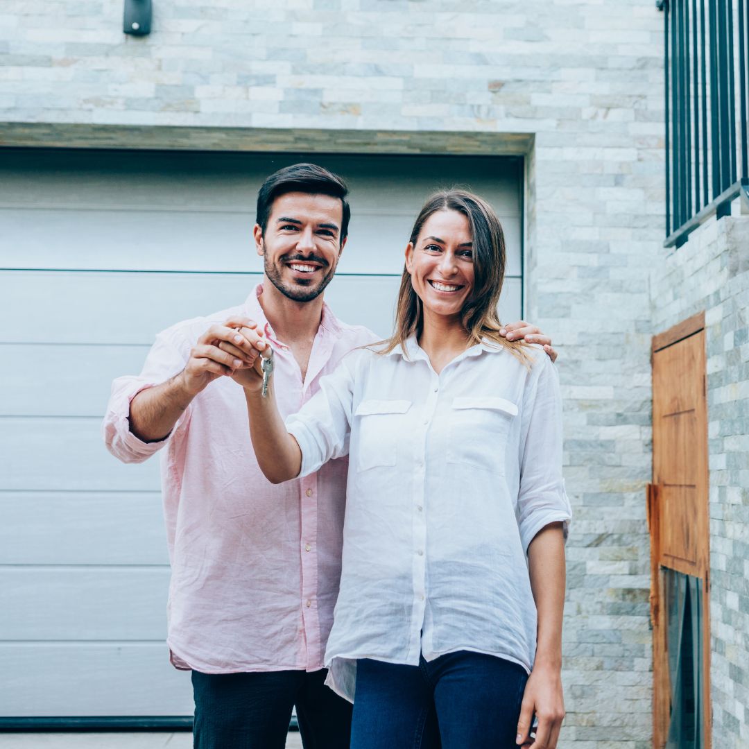 A young couple standing in front of their new house